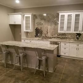 A modern kitchen with white cabinets, a light-colored marble island, a decorative backsplash, and metal stools.