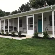 A white, single-story house featuring a screened-in porch with a black swing, a bright blue door, and a grassy front lawn.