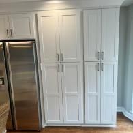 A stainless steel refrigerator sits next to a tall unit of white, shaker-style kitchen pantry cabinets.