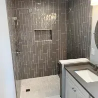 A modern bathroom with a gray vertical-tile shower stall featuring a recessed niche and a white vanity with a sink.