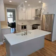 A bright modern kitchen with a gray island, white cabinets, stainless steel appliances, and wood floors.