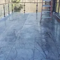 A balcony with glossy, blue-gray veined marble tiles, a metal railing, and a metal ladder standing near a brick wall.