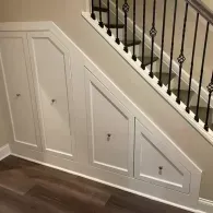 White custom cabinetry built under a staircase with four doors, each featuring a small decorative knob.