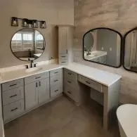 A bathroom vanity with gray cabinets, white countertops, two mirrors, and a makeup station against a wood-paneled wall.