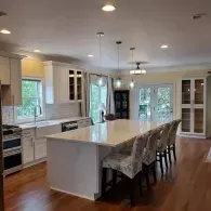 A bright, modern kitchen with white cabinets, a large center island with four chairs, and hardwood flooring.