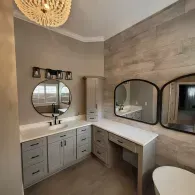 A bathroom vanity with gray cabinets, white countertops, two arched mirrors, a light fixture, and textured wall tiles.
