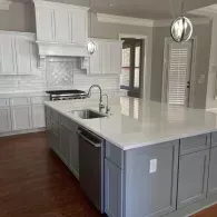A modern kitchen with a large central island, light-colored cabinets, stainless steel appliances, and wood flooring.