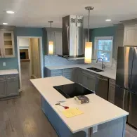 A modern, bright kitchen featuring a white center island, gray cabinetry, stainless steel appliances, and teal walls.
