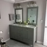 A double-sink bathroom vanity with gray cabinets, marble-look countertop, two mirrors, and light fixtures.