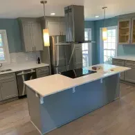 Modern kitchen with gray cabinets, white countertops, a central island with a cooktop, and stainless steel appliances.