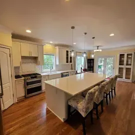 A bright, modern kitchen featuring white cabinets, a large central island with bar stools, and warm hardwood floors.