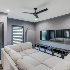 A modern media room featuring a light-colored sectional sofa facing a wall-mounted TV with a dark grey console below.