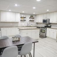 A modern kitchen featuring white cabinets, a central island, a dining table with chairs, and stainless steel appliances.