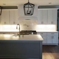 A modern kitchen featuring white cabinets, a large gray island, white countertops, and a black lantern-style pendant light.