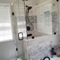 A modern bathroom shower with a glass enclosure, gray marble subway tile, and a matte black shower head and handle.