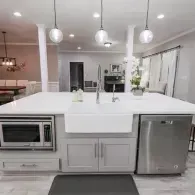 Modern kitchen island with a white farmhouse sink, stainless steel microwave and dishwasher, and three pendant lights.