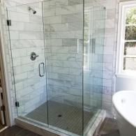 A glass-enclosed shower with white marble-style subway tile walls and a dark gray mosaic tile floor next to a bathtub.