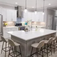 Modern kitchen with a large island, gray cabinets, white countertops, four bar stools, and stainless steel appliances.