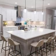 Modern kitchen with a large gray island, white cabinets, stainless steel appliances, and four bar stools.