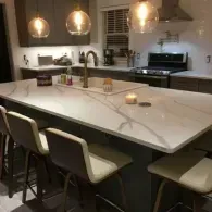 A modern kitchen island with white veined countertops, three bar stools, and three pendant lights hanging above.