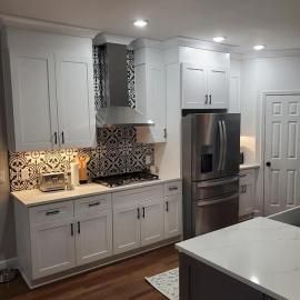 A bright kitchen with white shaker cabinets, stainless steel appliances, and a patterned tile backsplash.