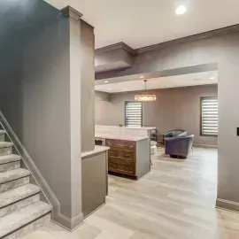 A staircase with gray carpet leads to a modern, open-concept living area with gray walls, wood flooring, and an island.