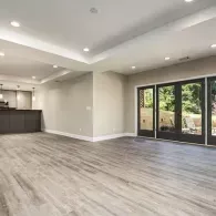 An unfurnished room with light gray wood-look flooring, neutral walls, recessed lighting, and glass patio doors.