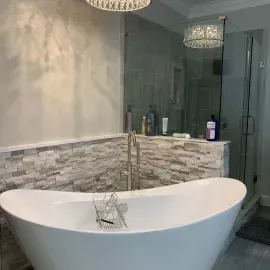 A modern bathroom featuring a white soaking tub in front of a stone tile wall and a glass-enclosed shower.