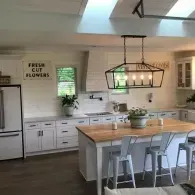 A bright, modern farmhouse kitchen with a large wooden island, industrial pendant lighting, and white cabinetry.