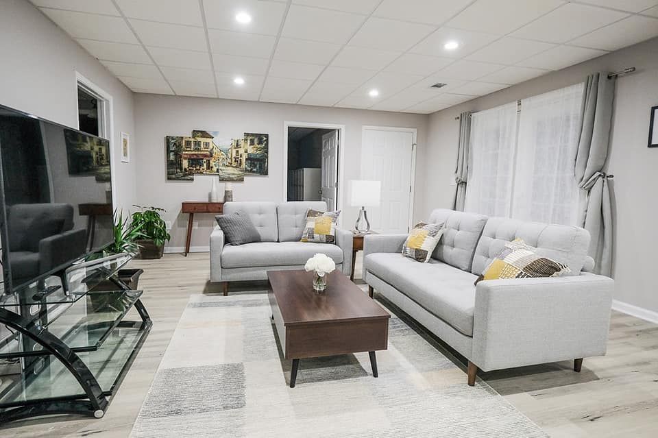 A living room with light gray sofas, a dark coffee table, a white rug, and a television on a glass stand.