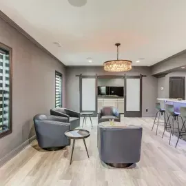 Modern lounge with grey swivel chairs, small side tables, a bar counter, and a crystal chandelier in a neutral room.