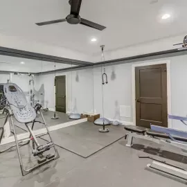 A home gym featuring workout equipment, a large wall mirror, a ceiling fan, and a brown door.
