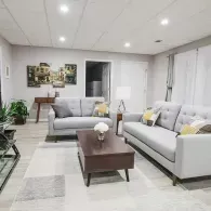 Modern living room with grey sofas, a dark wood coffee table, neutral rug, and wall art in a brightly lit space.