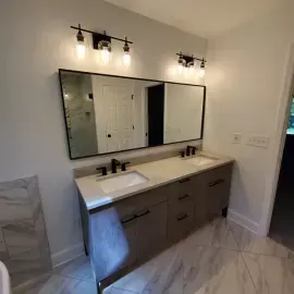 A modern bathroom vanity with dual sinks, dark wood cabinets, a large mirror, and two black industrial-style light fixtures.