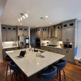 A modern kitchen with light gray cabinetry, a white marble island, and blue stools under recessed lighting.