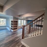 A staircase leads to a room with light wood floors, built-in shelving, and windows.
