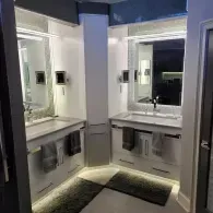 A modern double vanity bathroom with white cabinets, large mirrors, and soft under-cabinet lighting.