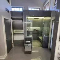 A modern gray bathroom with a glass-enclosed shower, a built-in bathtub, and minimalist cabinetry under bright lighting.