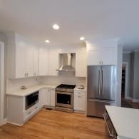 Modern white kitchen with stainless steel appliances, wood flooring, and recessed lighting.
