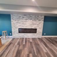 A room with a white stone fireplace wall, teal painted side walls, and light brown wood-look flooring.