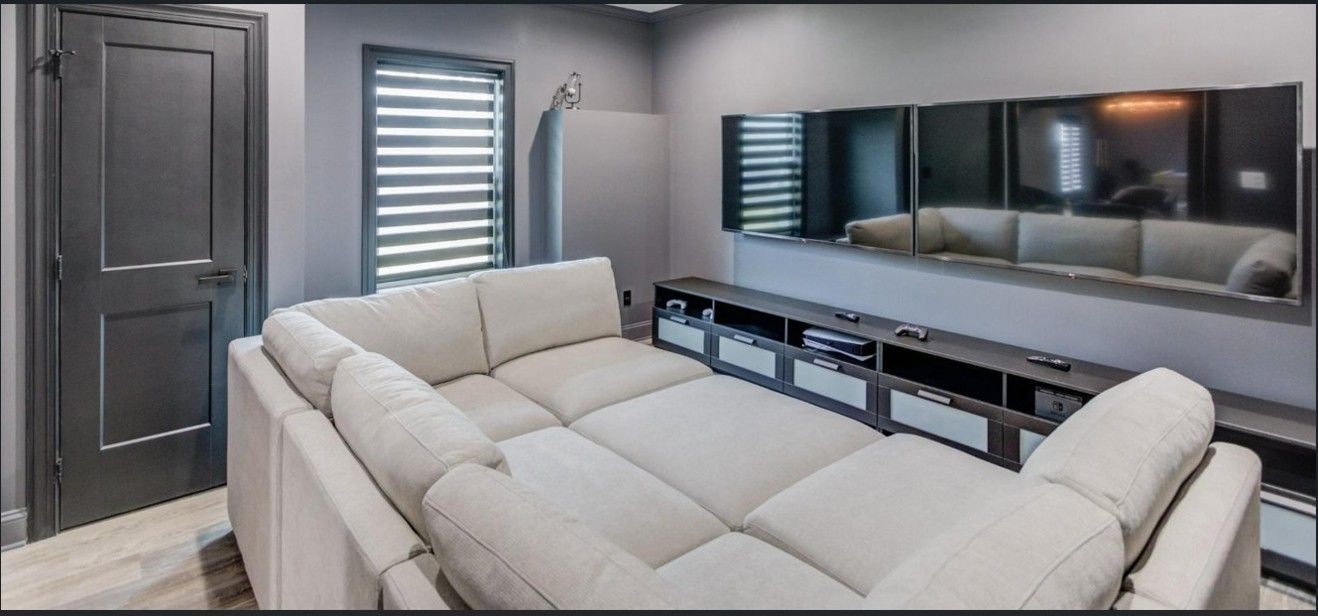 A cozy home theater with a large, light-colored sectional sofa facing a wall-mounted television and a media console.