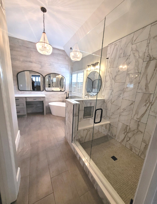 A modern bathroom featuring a glass-enclosed shower, a freestanding bathtub, double vanity with mirrors, and a chandelier.
