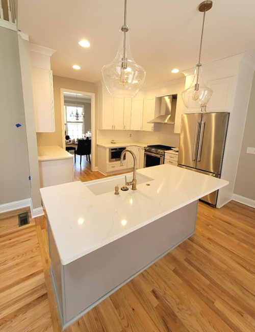 A bright, modern kitchen featuring a large white island, stainless steel appliances, white cabinets, and hardwood floors.