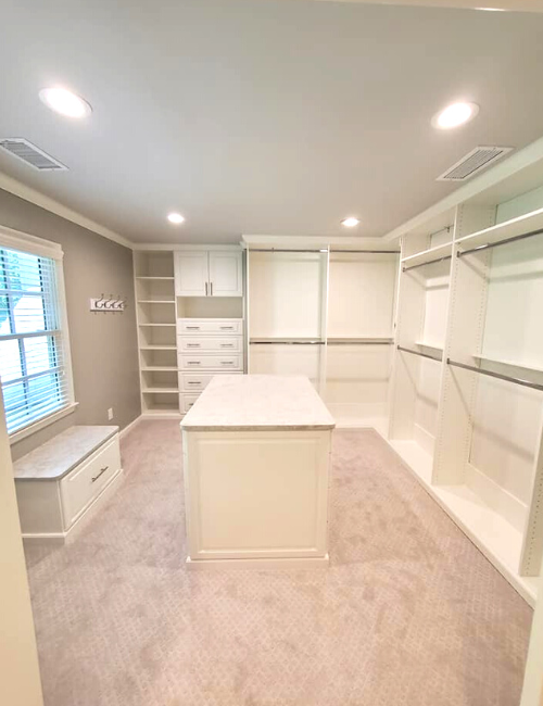 A walk-in closet featuring white cabinetry, a center island, wall-to-wall carpeting, and a window seat.