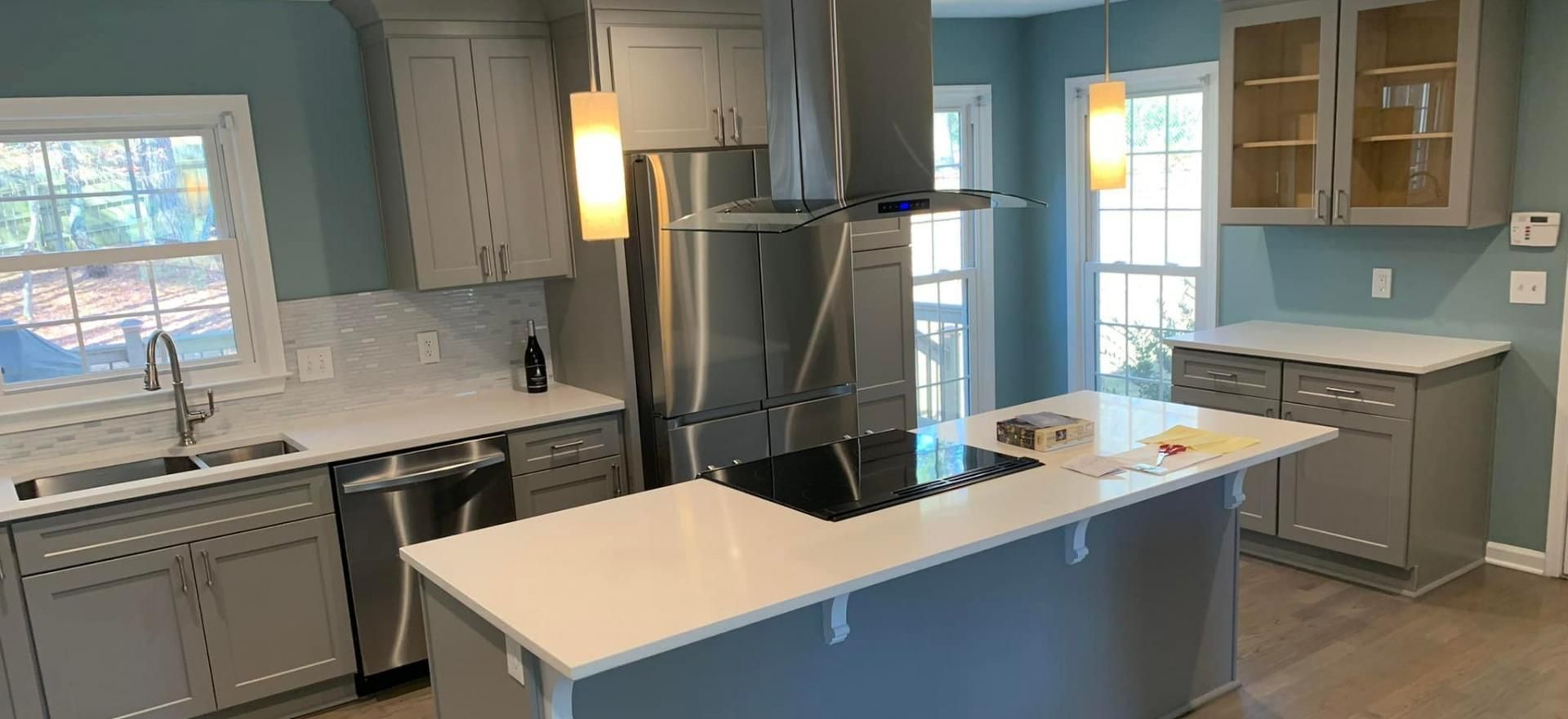 Modern kitchen with grey cabinets, white countertops, stainless steel appliances, and two hanging lights over an island.
