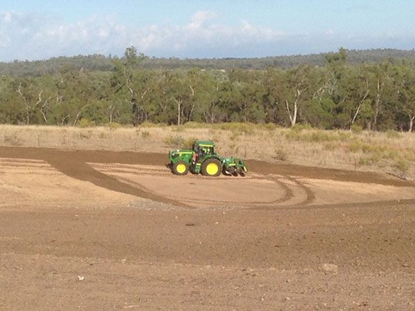 A green tractor is driving down a dirt road.