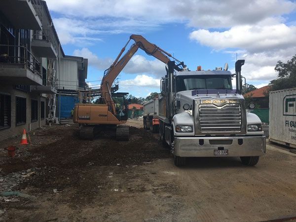 A large truck is driving down a dirt road next to a large excavator.