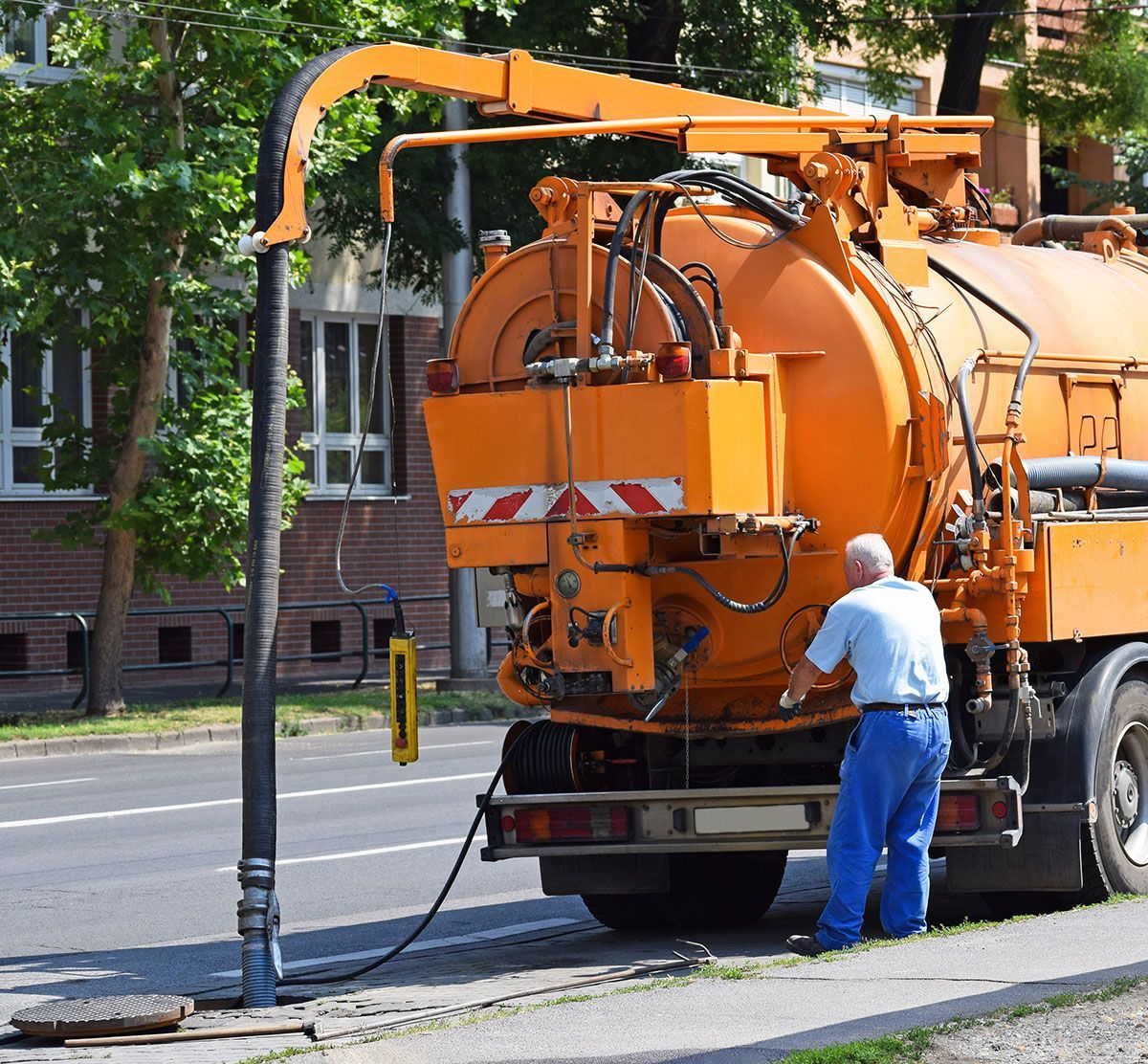 A man is standing next to an orange vacuum truck on the side of the road.