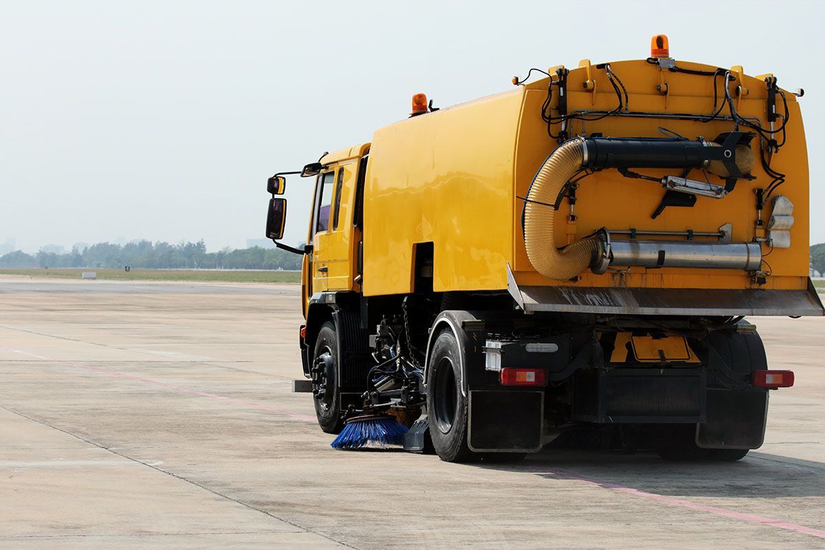 A yellow truck is parked on the side of an airport runway.