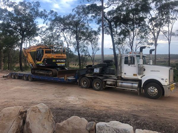 A truck is carrying a yellow excavator on a flatbed trailer.
